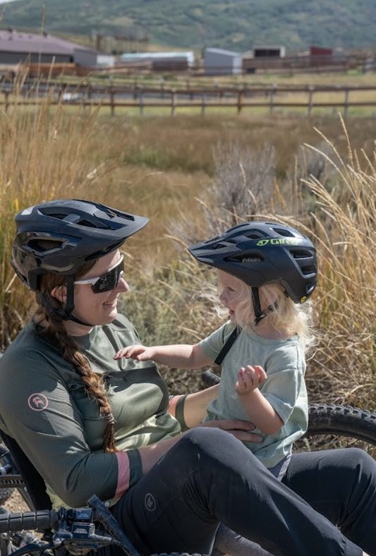 "Amana sitting on her adaptive bike while holding Zoey"
