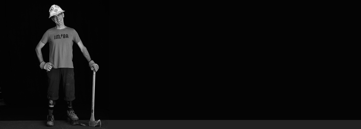 IMBA Trail Solutions staff member Chris Orr smiling while leaning against a handtool used in trailbuilding