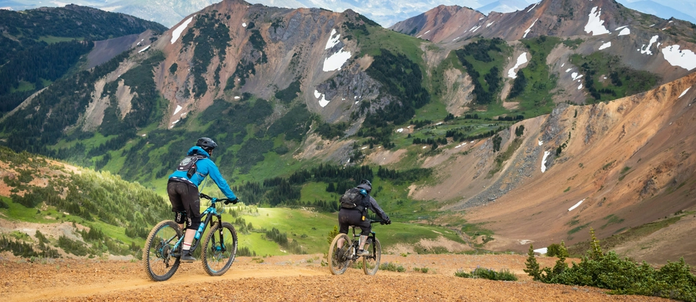 Two mountain bikers descend a trail toward a valley
