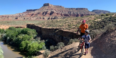 Man and Child walking bikes along singletrack trail on public lands near Hurricane Cliffs Trail System in Utah.