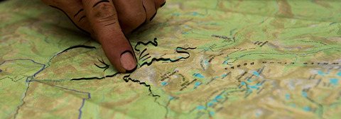 photo of a finger pointing at a map, with illustrated details added