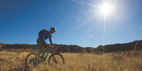 a mountain biker standing up riding on singletrack in a grassy field on public lands. |