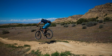 Demonstrating progress, a mountain biker is pictured mid-jump on southwestern public lands singletrack. 