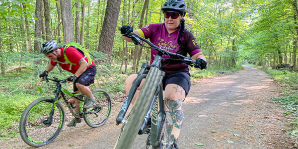 Two mountain bikers riding on a doubletrack trail. Female mountain biker popping a sick wheelie. 