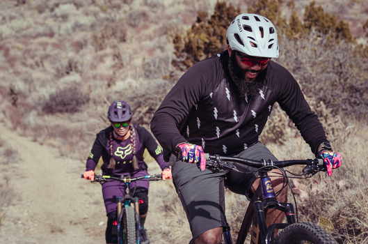 Two people smiling riding bikes on trails